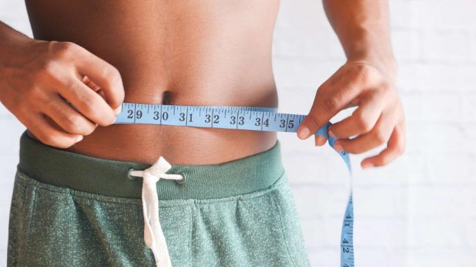 Tour de taille jeune homme short vert qui tient un mètre ruban bleu