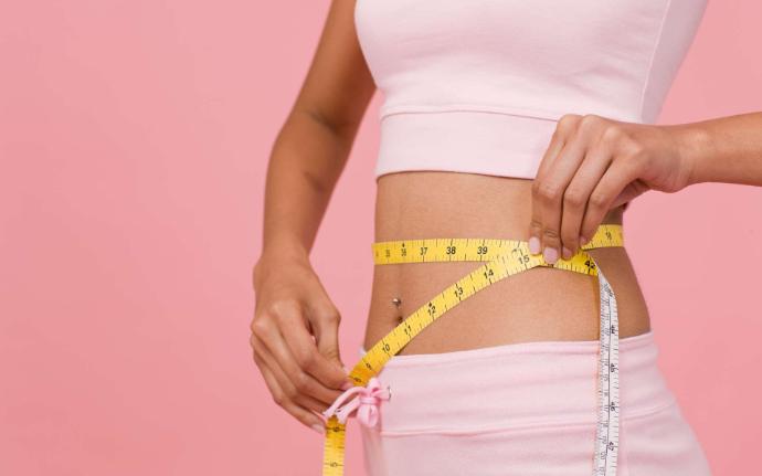 Femme haut et bas rose sui tient un mètre ruban jaune autour de sa taille sur fond rose