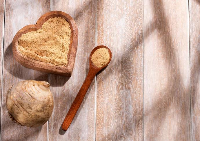 racine de maca et maca en poudre dans une cuillère en bois et un récipient en bois en forme de coeur sur une table en bois plus clair