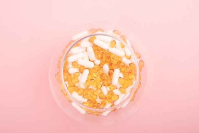 Compléments alimentaires jaunes et blancs dans un récipient en verre vu de haut sur fond rose
