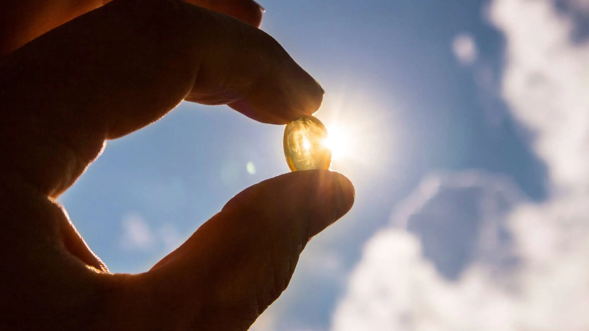 Main tenant un complément alimentaire face au soleil avec ciel bleu et nuages blancs en arrière-plan