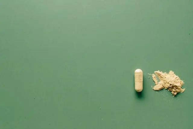 Gélule beige complément alimentaire avec poudre beige à côté sur fond vert 
