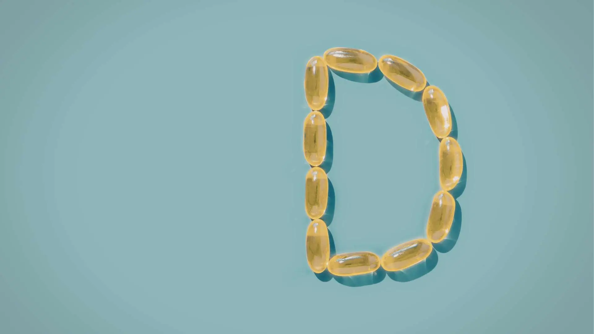 Lettre D formée avec des gélules compléments alimentaires jaunes sur fond turquoise