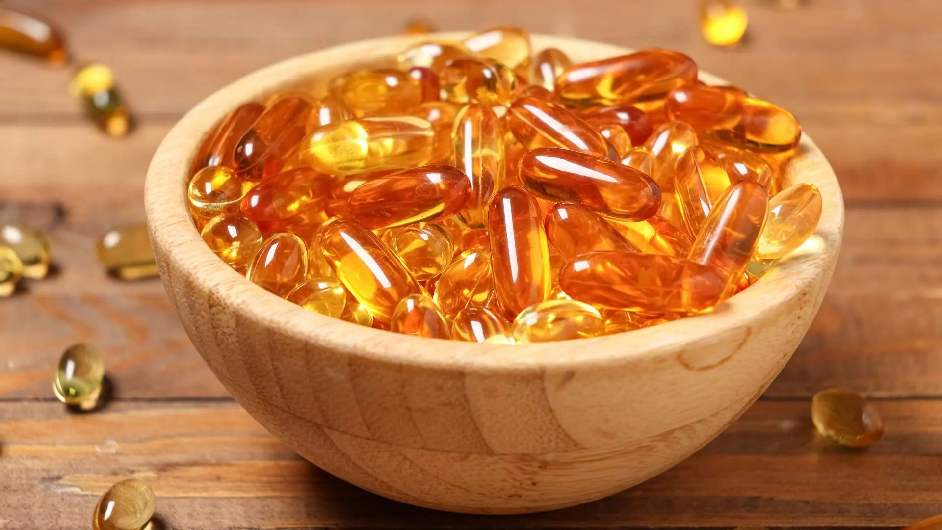 Gélules orangées compléments alimentaires dans bol en bois sur table en bois avec des gélules autour