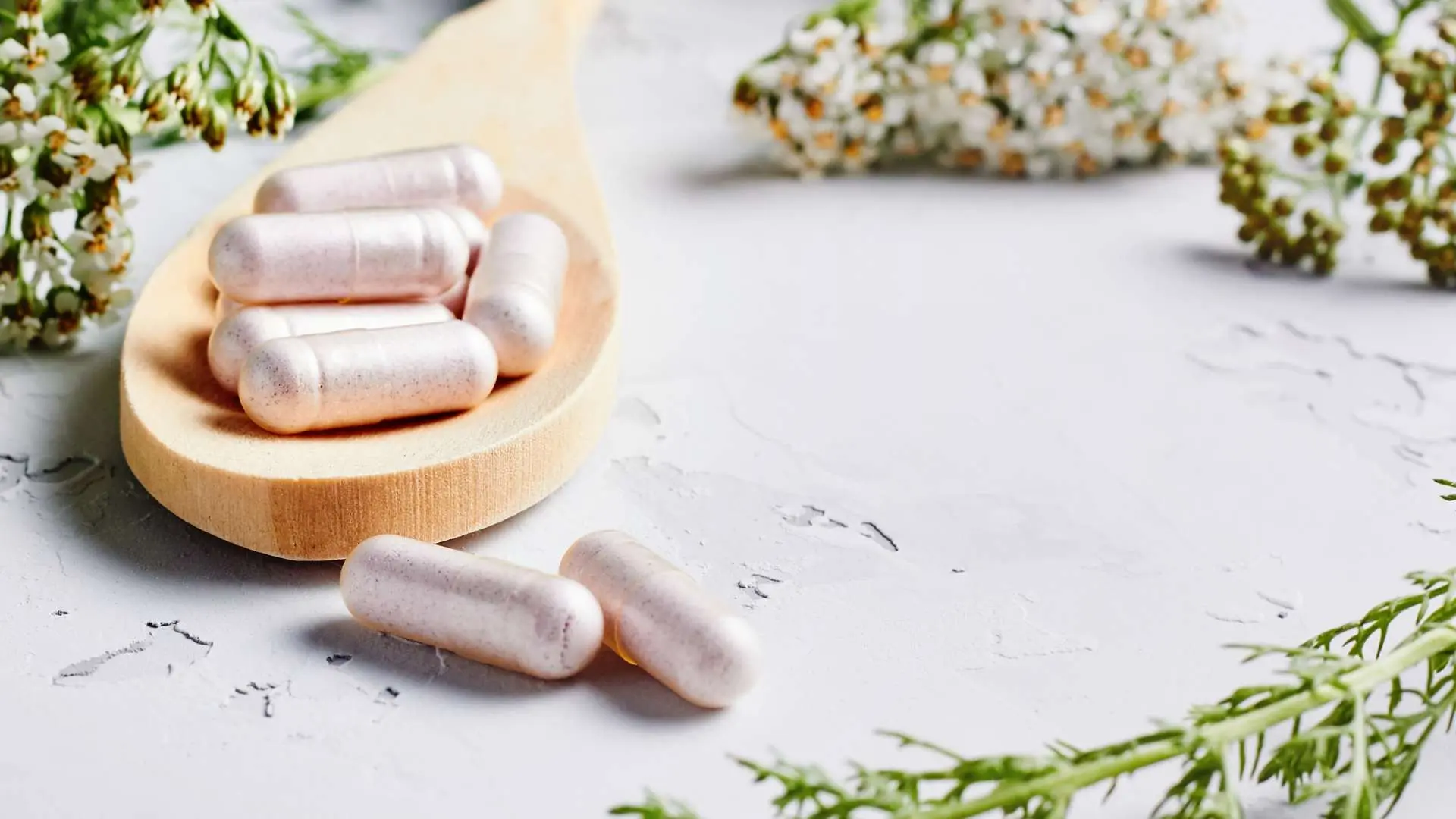 Compléments alimentaires gélules blanches dans cuillère en bois avec fleurs d'aubépine derrière