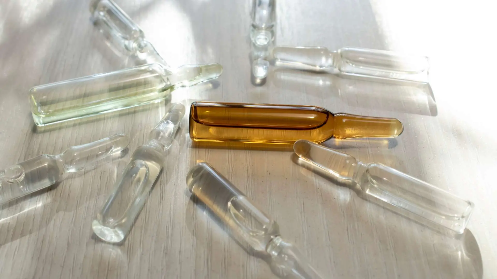 Ampoules unidoses compléments alimentaires sur une table en bois clair avec rayons de soleil