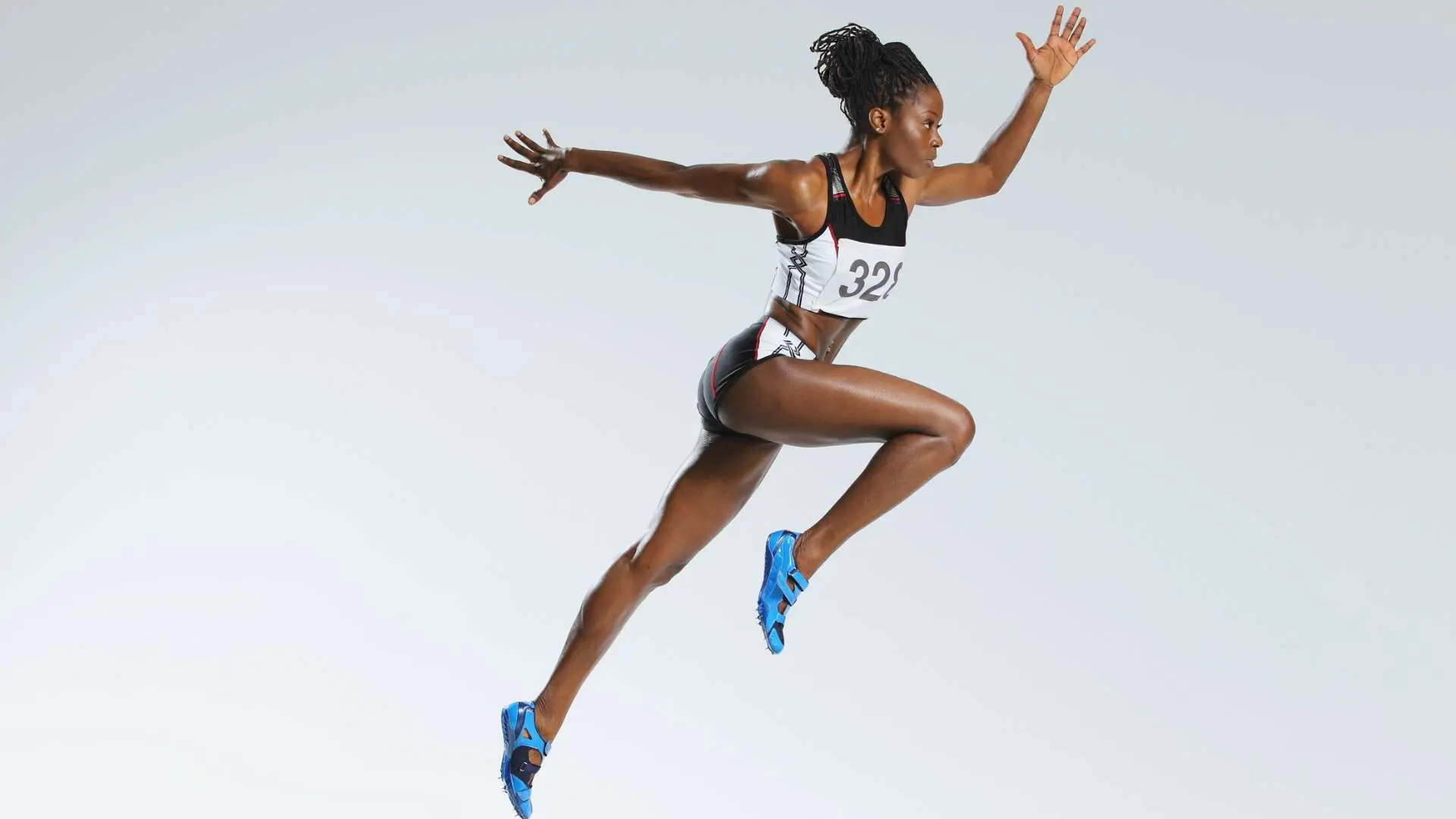 Femme noire athlète en plein saut sur fond gris clair